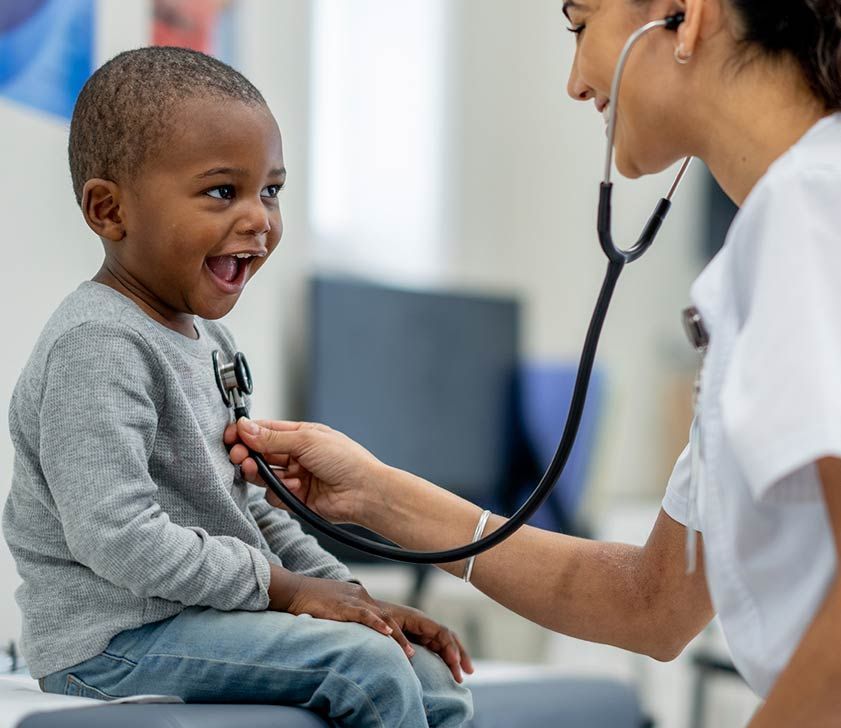 Doctor using a stethoscope to examine a smiling child in a clinic