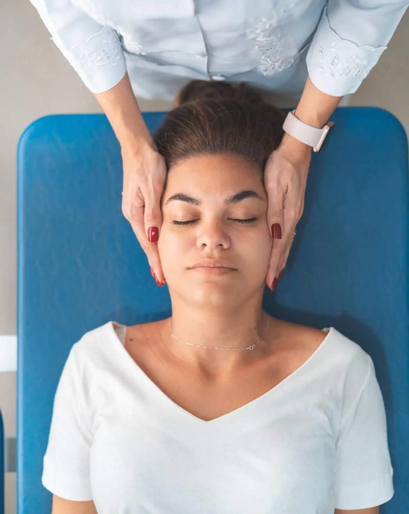 Woman receiving a head massage while lying on a blue treatment table