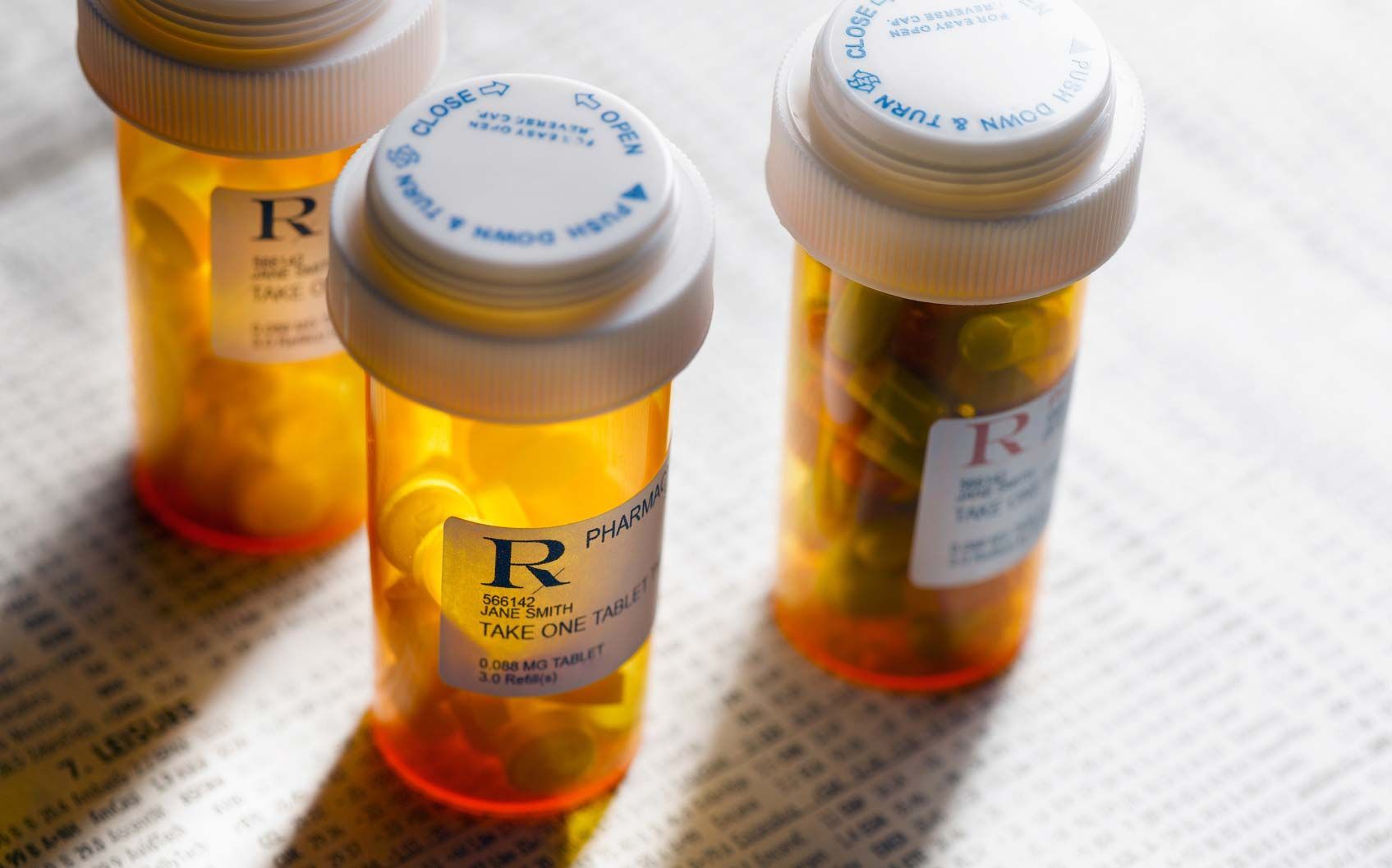 Three amber prescription pill bottles with white caps on a light surface, one lying sideways