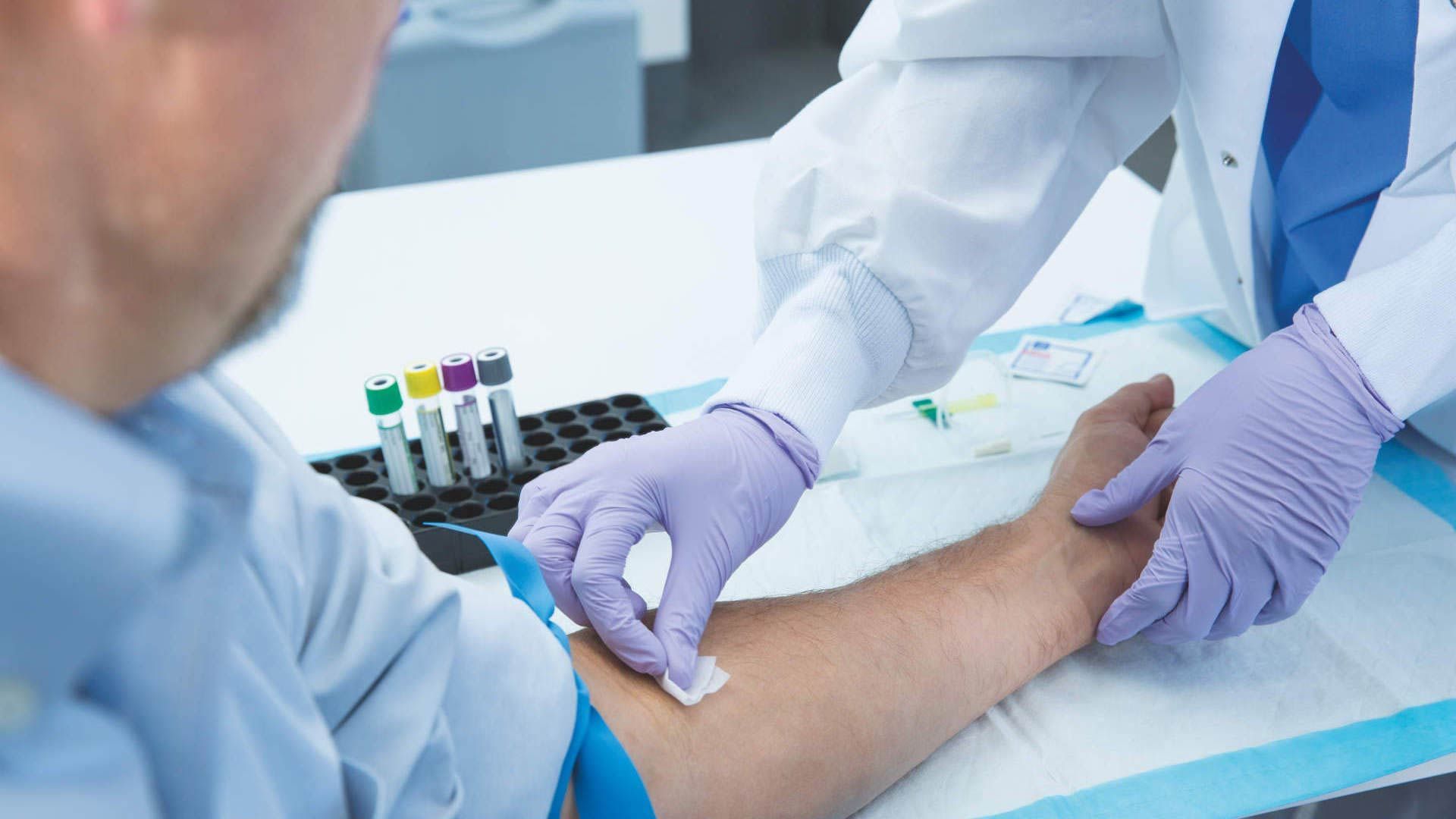 Healthcare worker drawing blood from a patient’s arm with a syringe in a clinical setting