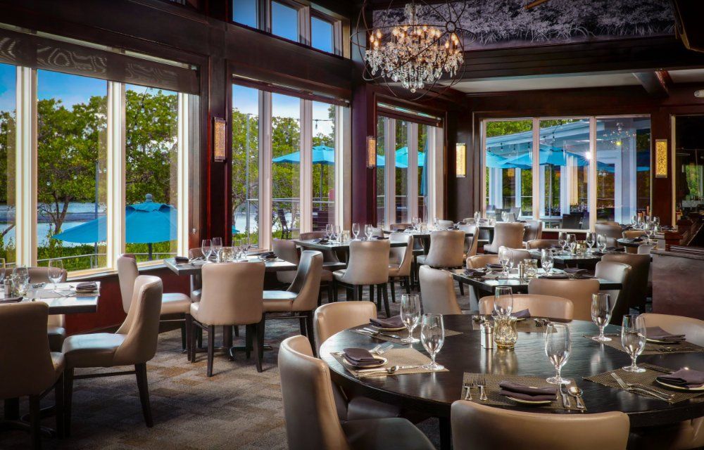 Elegant waterfront restaurant with set tables, chandeliers, and large windows overlooking the ocean