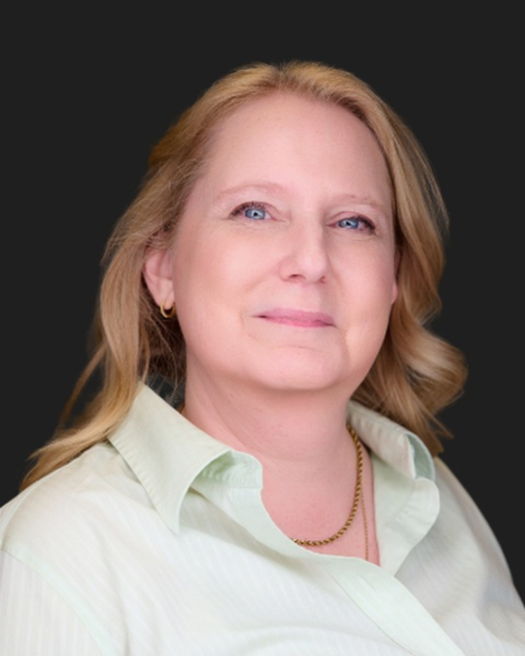Woman with long blonde hair, smiling in a modern office, wearing a light green shirt.