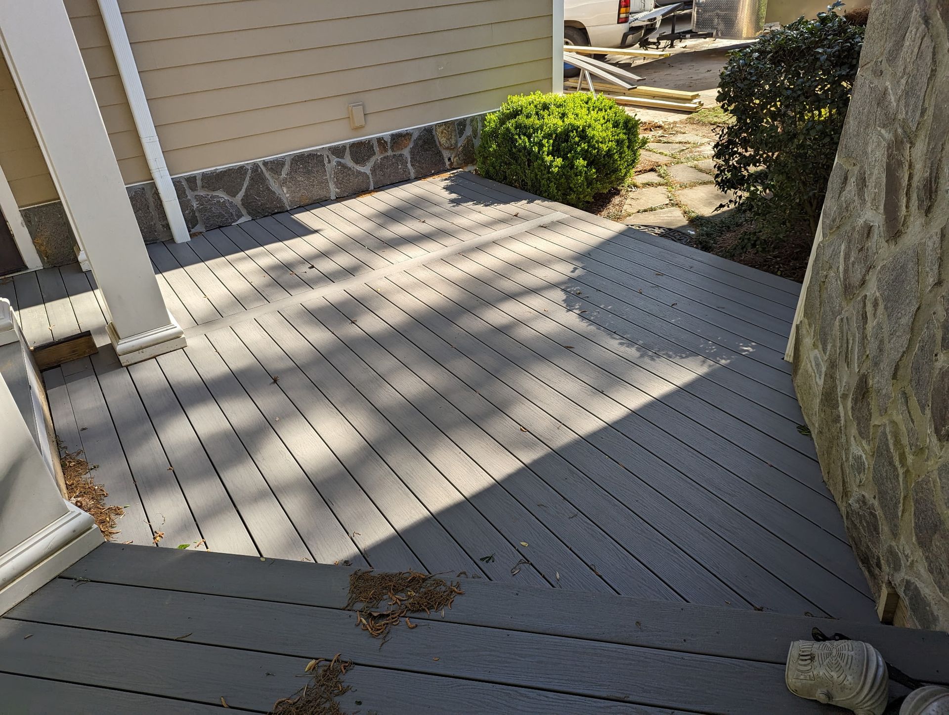 Gray composite deck with steps, next to a stone wall and house exterior.