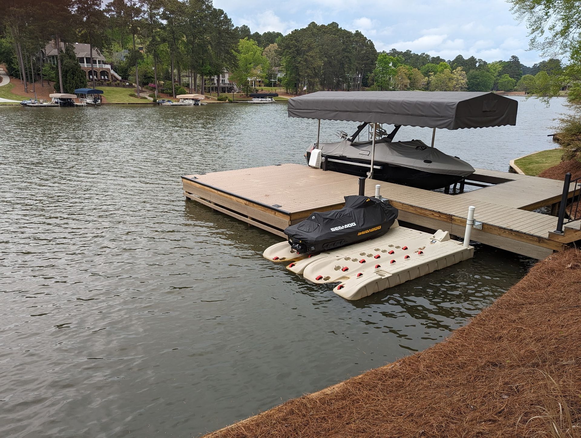 Dock on a lake with a covered boat lift holding a boat, and a jet ski on a smaller floating platform.