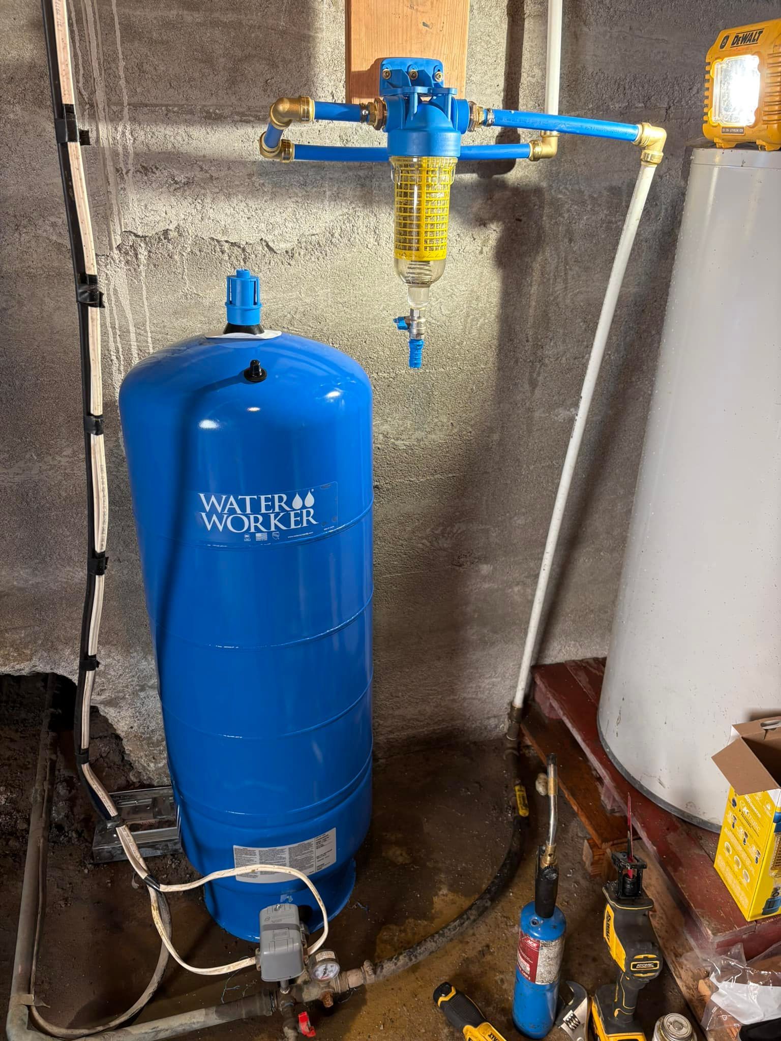 Blue water pressure tank with attached filter and plumbing in a basement setting.