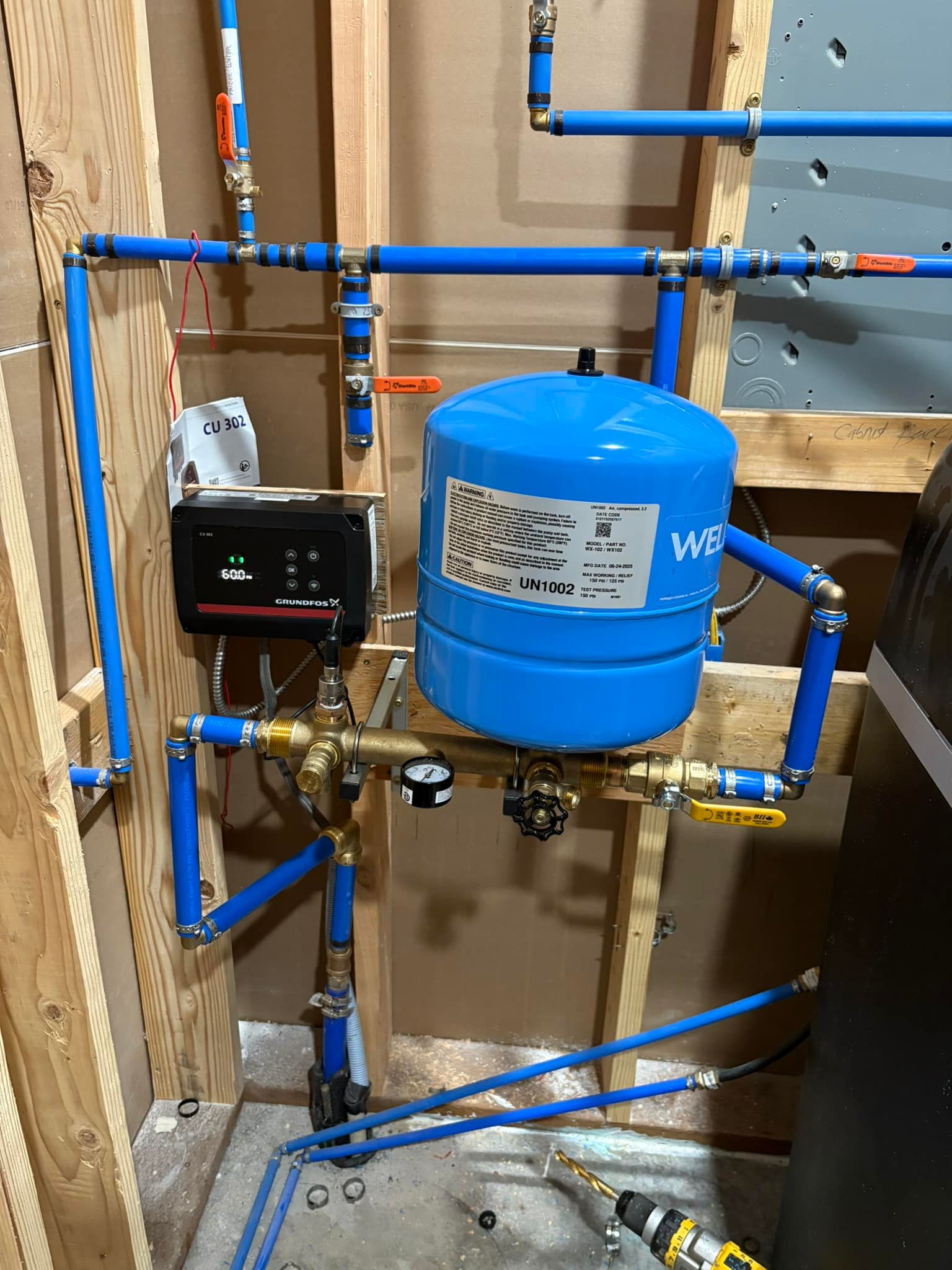 Blue and copper plumbing system with a blue pressure tank and black control box installed on a wooden wall.
