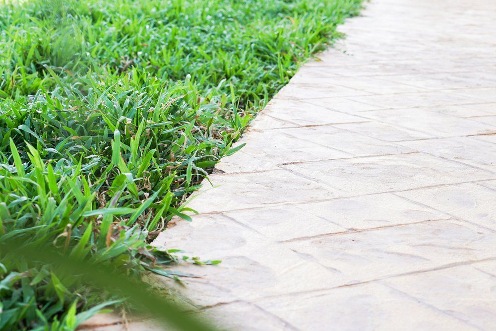 person kneeling on the ground by a stone pathway rolling out sod
