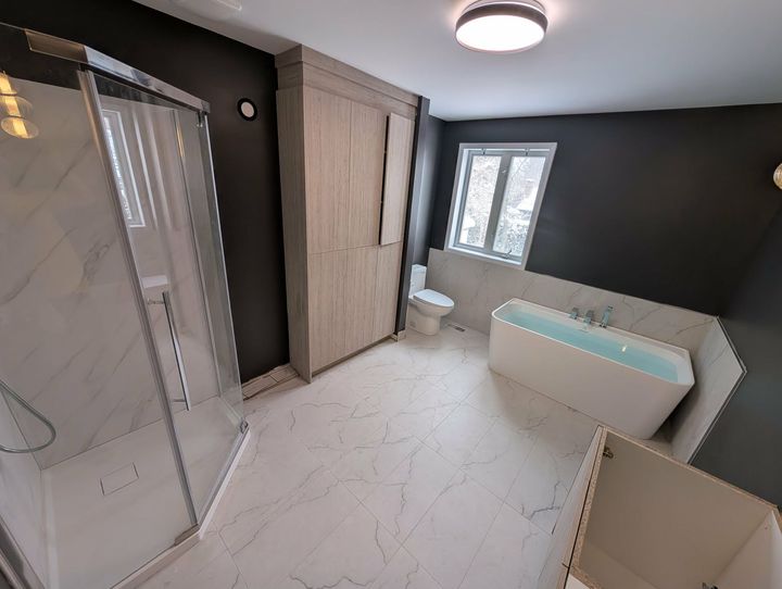 Salle de bains moderne avec douche, baignoire, toilettes et grand placard ; murs gris foncé, robinetterie blanche, placard en bois clair.