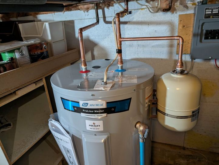 Un chauffe-eau avec des tuyaux en cuivre et un vase d'expansion dans une buanderie.