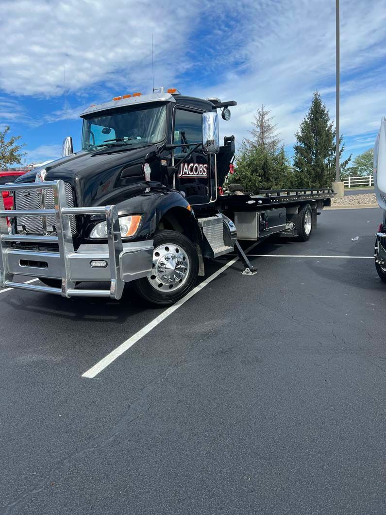 Black tow truck parked in a parking lot on a sunny day.
