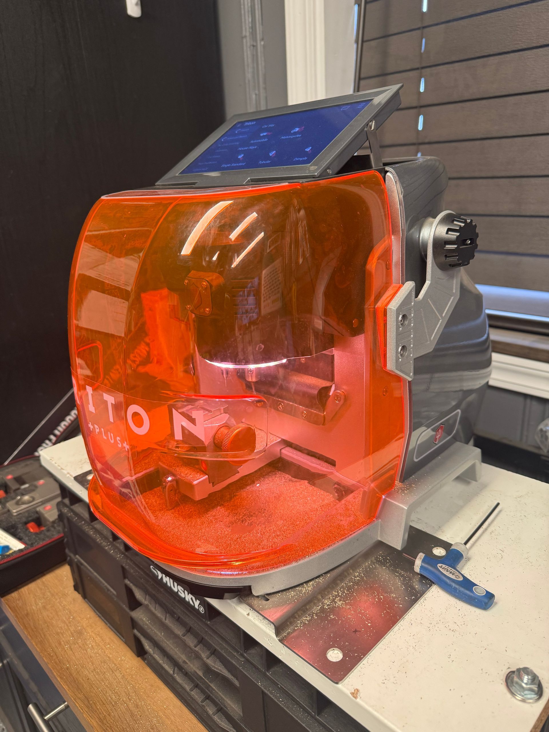 Orange key cutting machine with clear top, open for use, in a workshop.