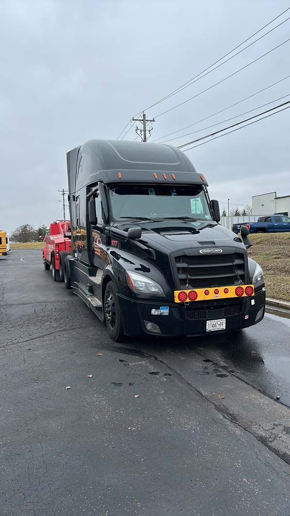 Black semi-truck parked on a road on an overcast day.