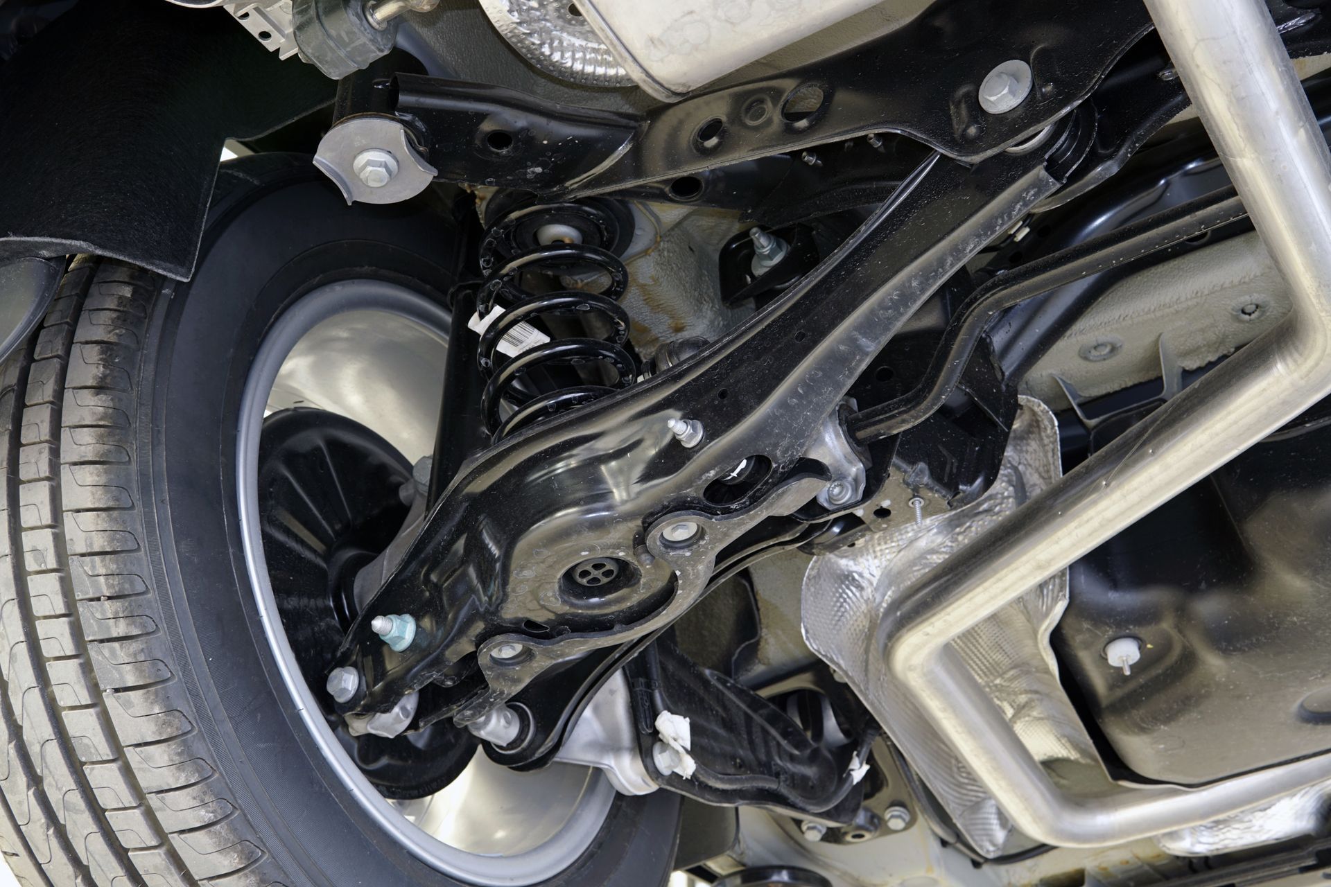 Underneath view of a black car suspension, with a tire, shock absorber, and various metal components.
