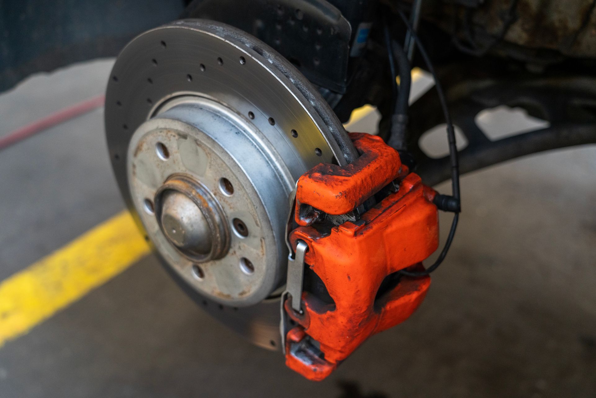 Orange brake caliper on a perforated disc brake, attached to a vehicle's wheel assembly.