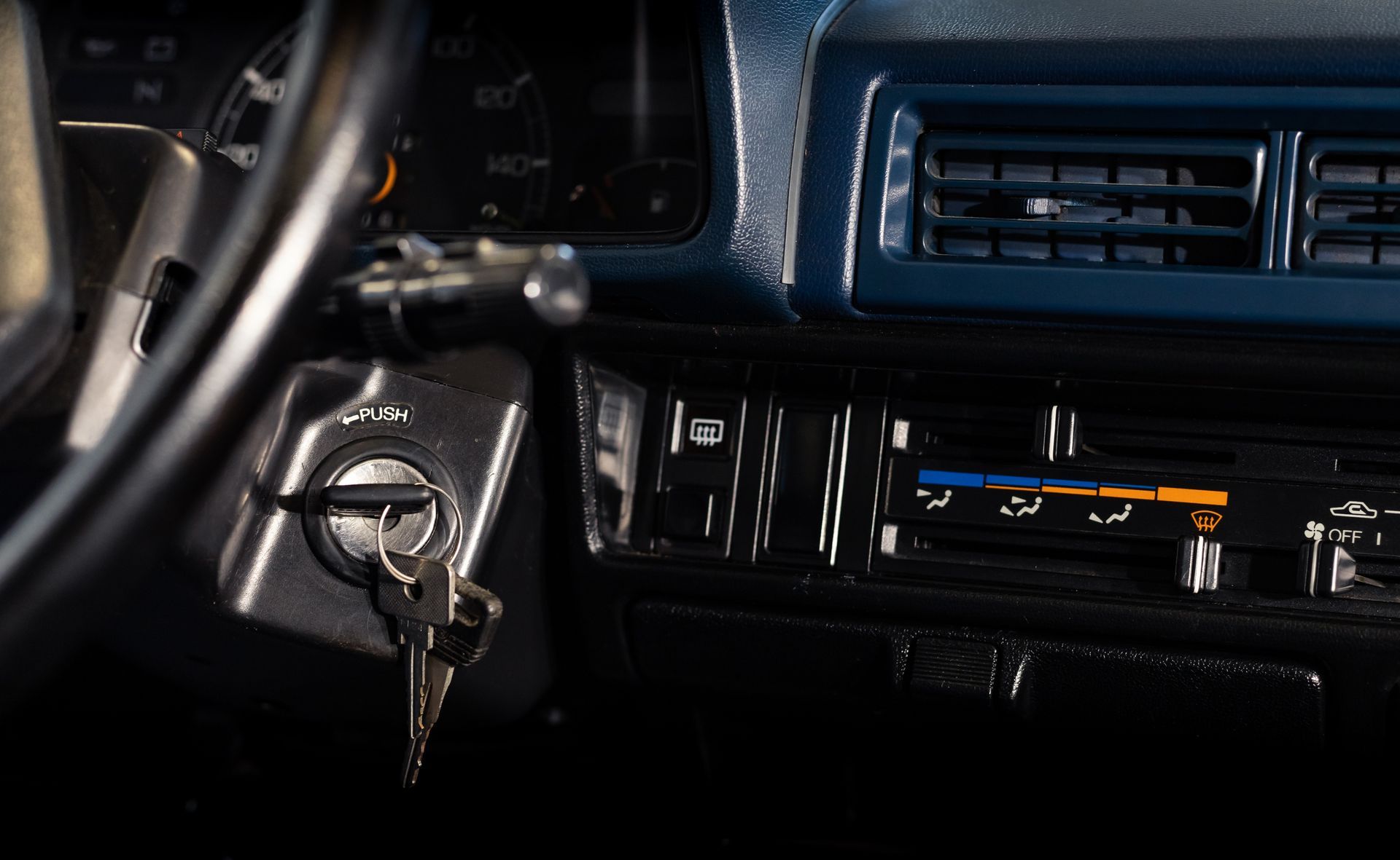 Dashboard of a vintage car with keys in the ignition, showing gauges, air vents, and temperature controls.