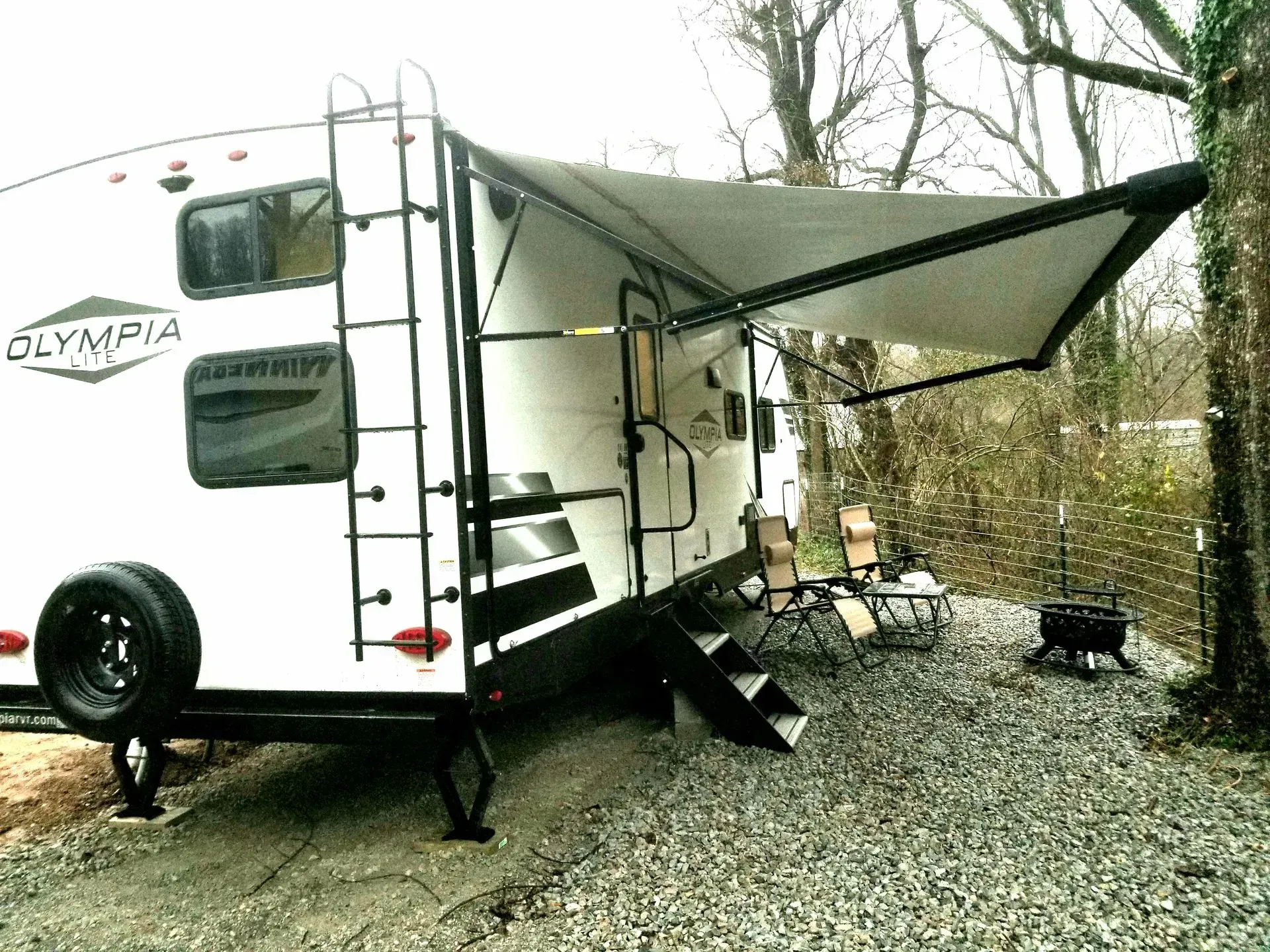 A white rv with a canopy is parked in a gravel lot.
