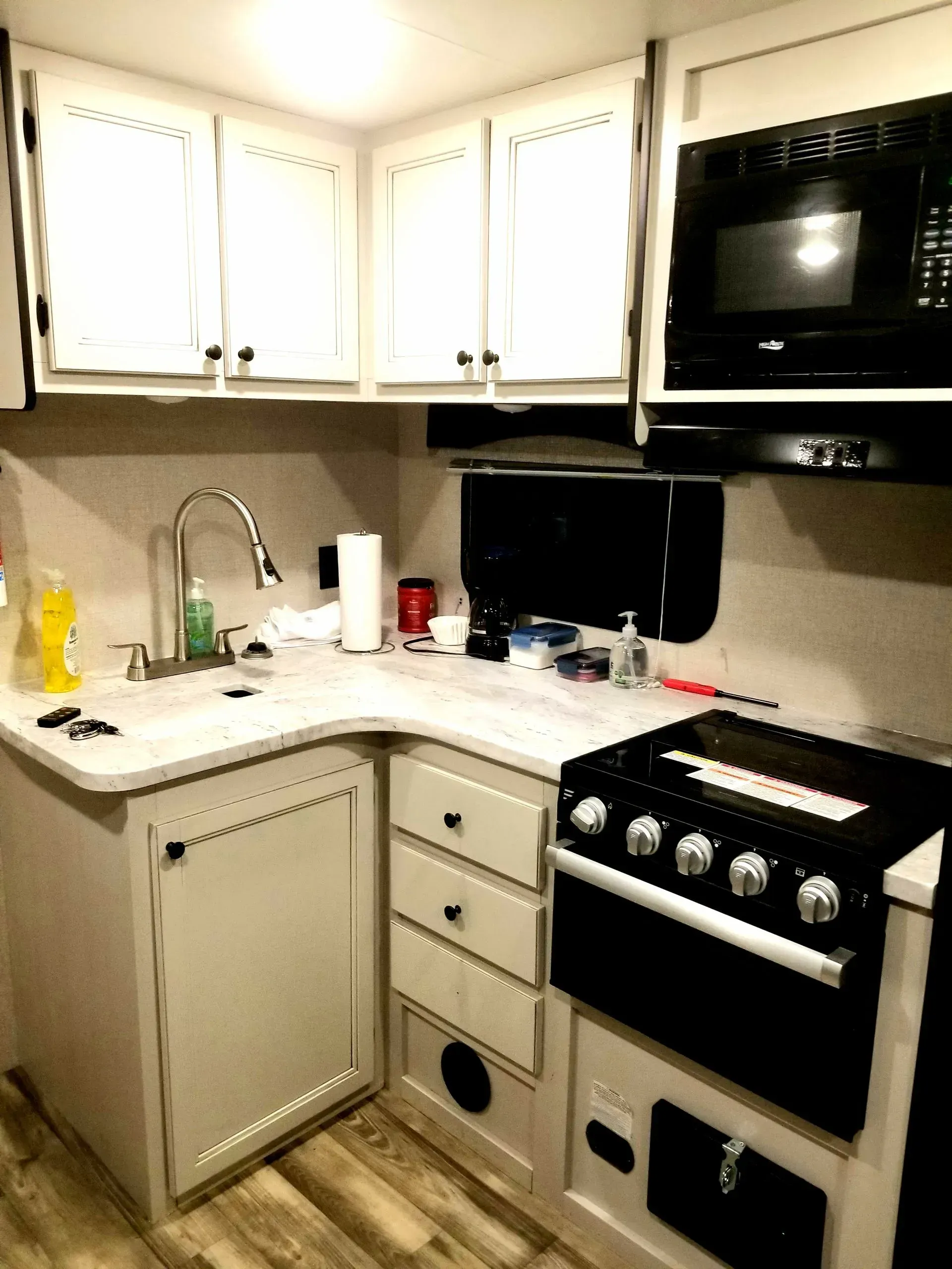A kitchen with white cabinets , a stove , a sink , and a microwave.