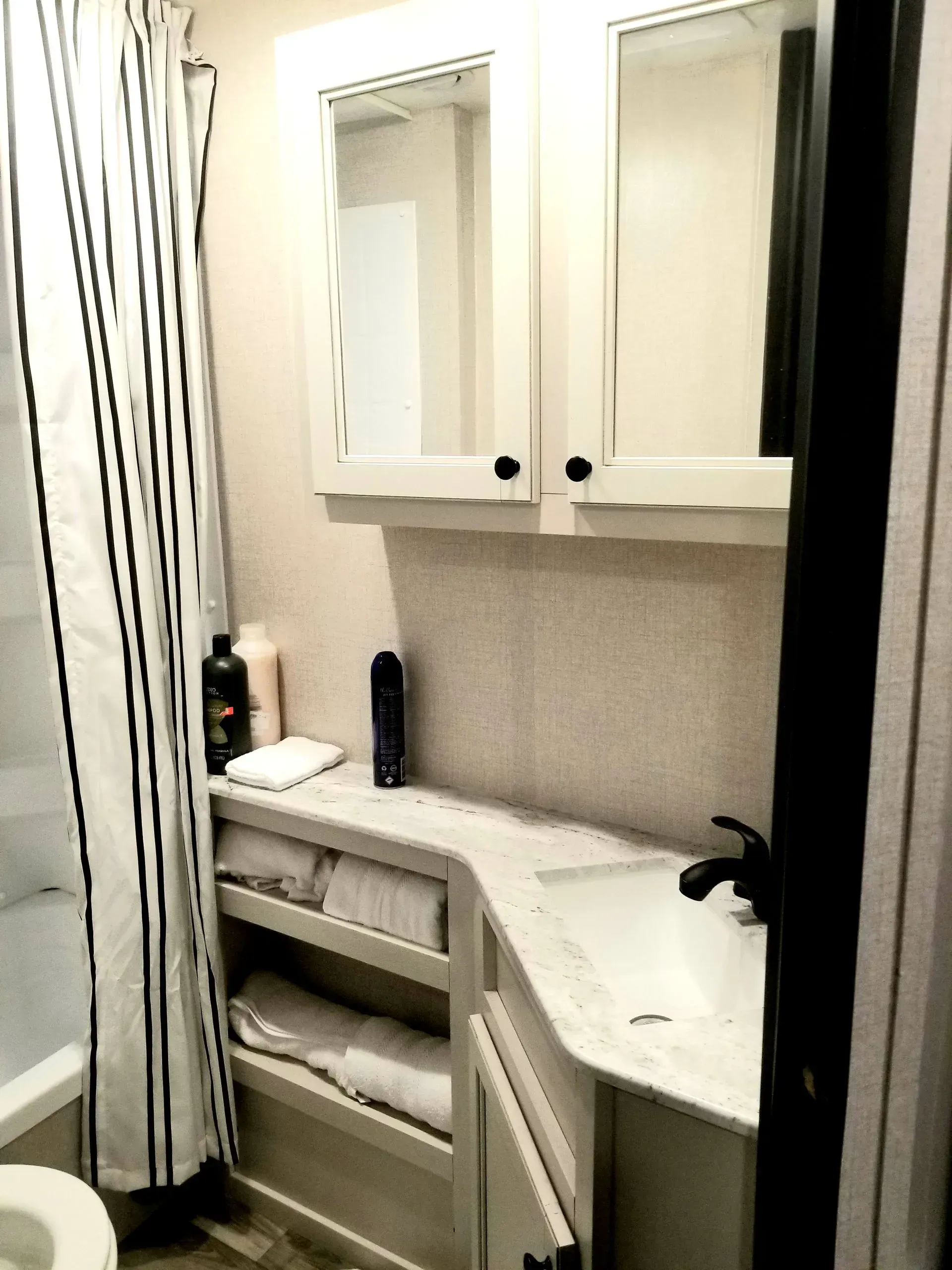 A bathroom with a toilet , sink , mirror and shower curtain.
