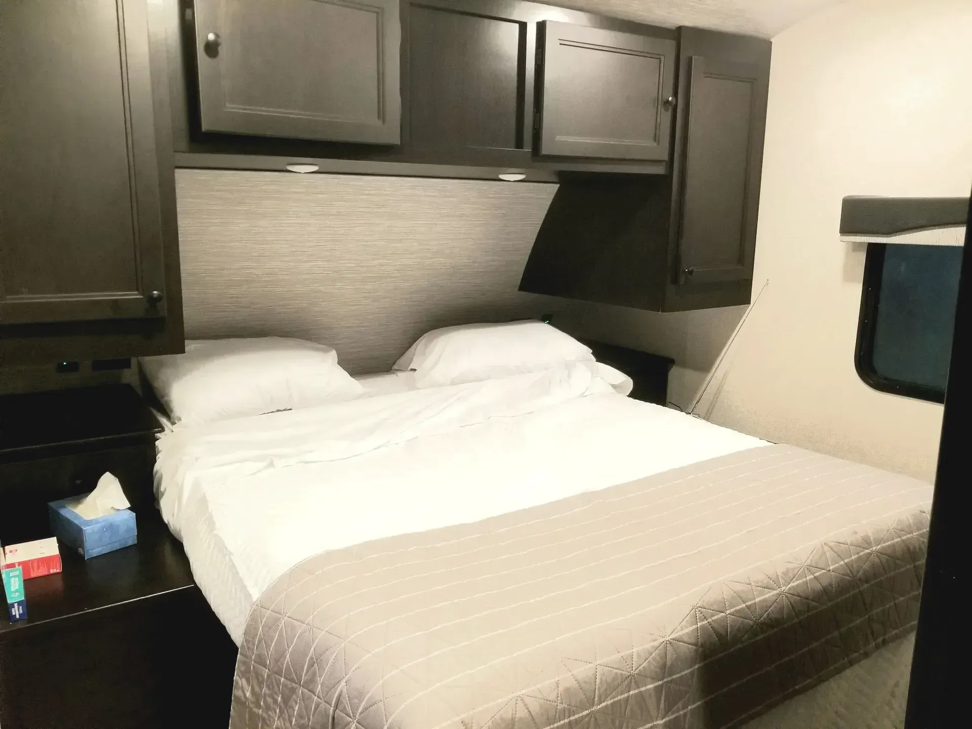 rv bedroom with a bed , nightstand , cabinets and a box of tissues.