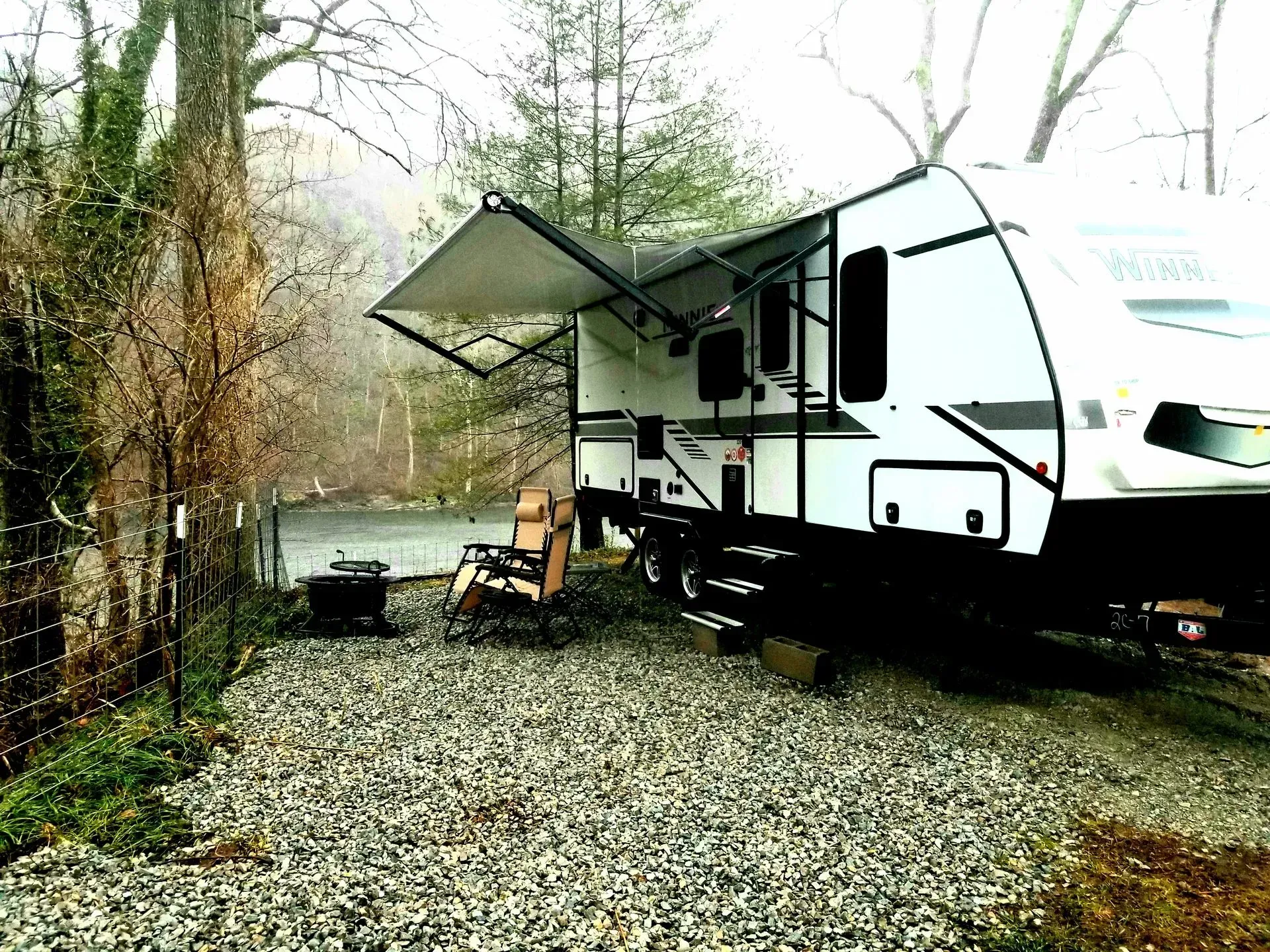 A rv is parked in a gravel lot next to a river.