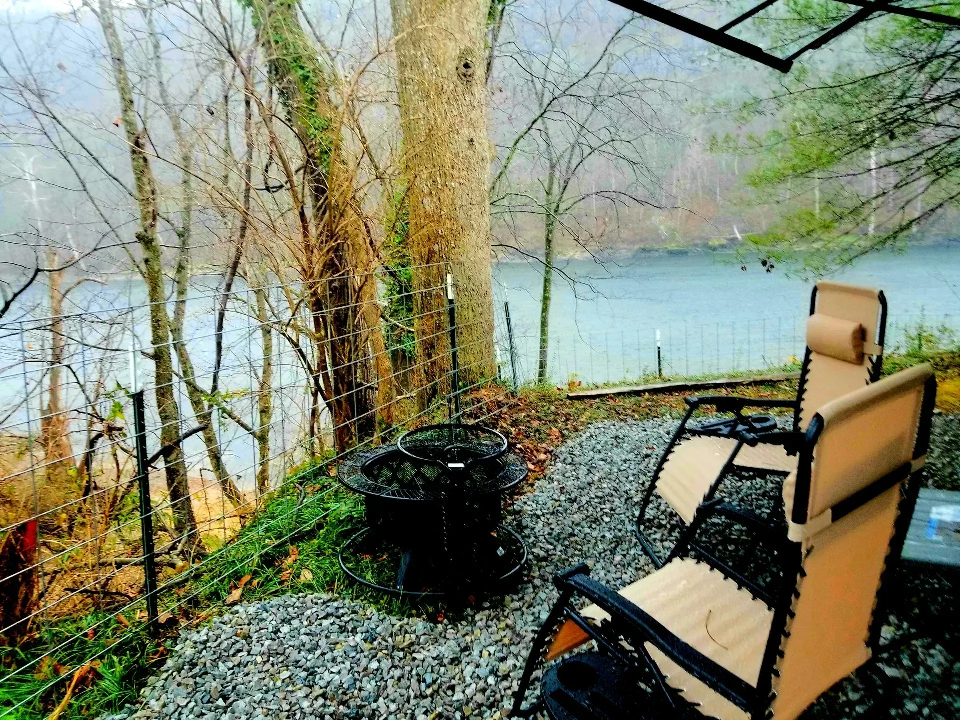 Two chairs are sitting on a gravel patio overlooking a lake.