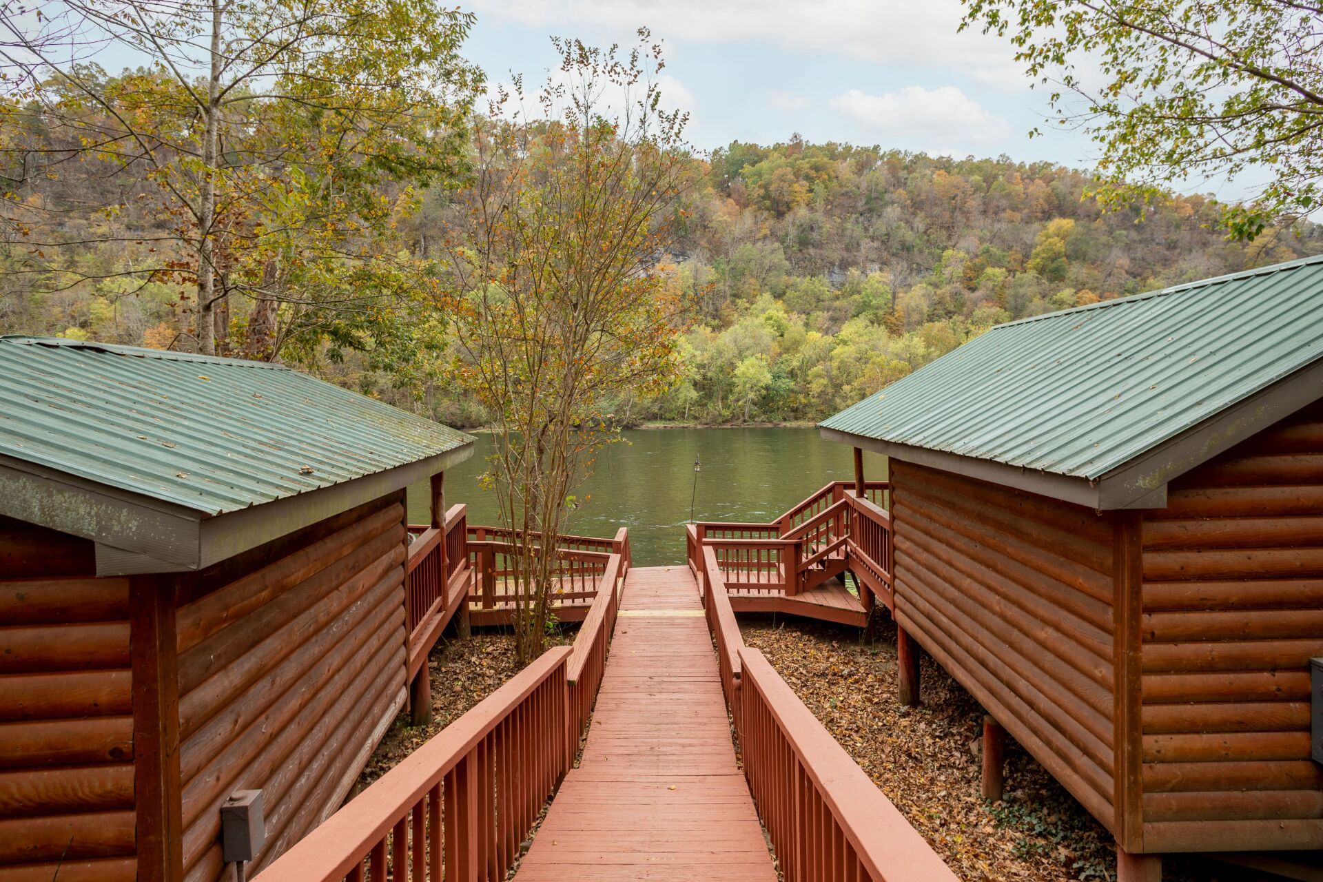 A wooden walkway leading to a lake between two log cabins.