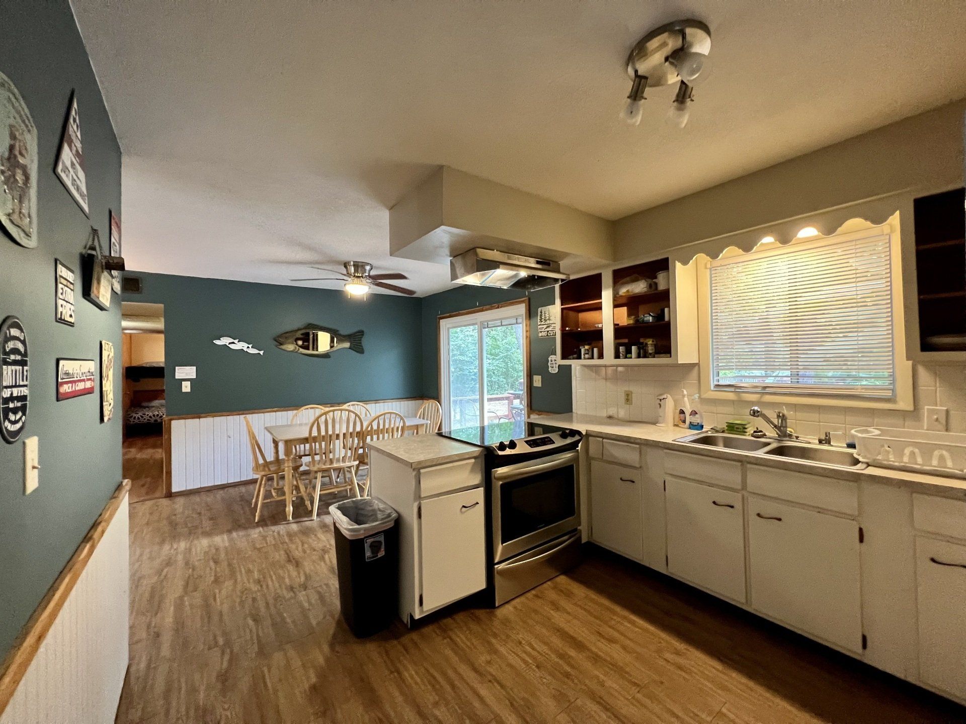 The Cottage kitchen with white cabinets , a stove , a sink , and a trash can.