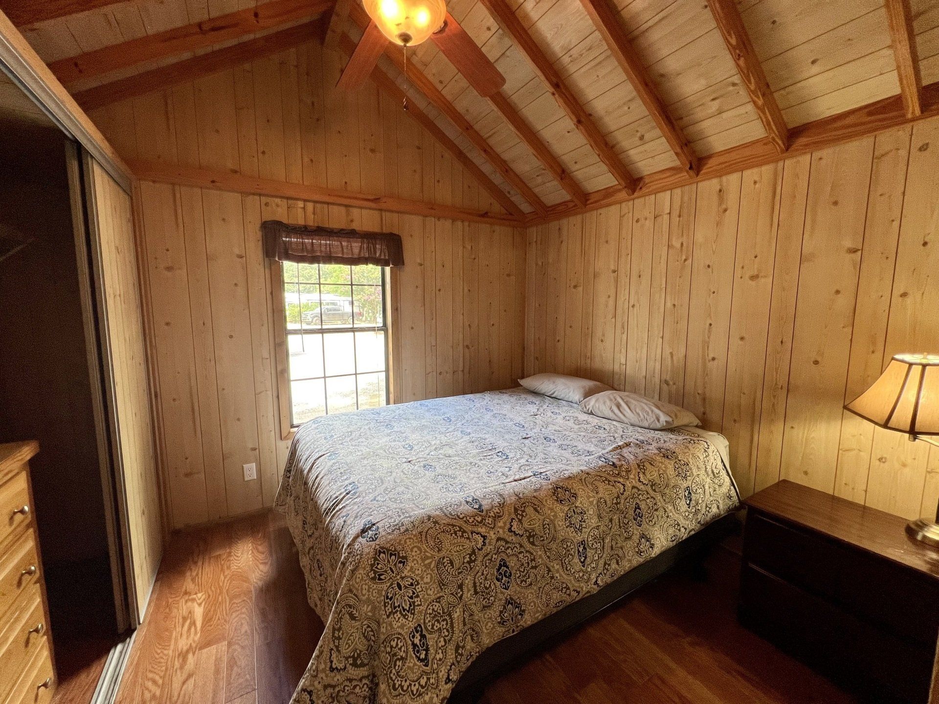bedroom with a bed , nightstand , lamp and window in humpy fly cabin at copper johns