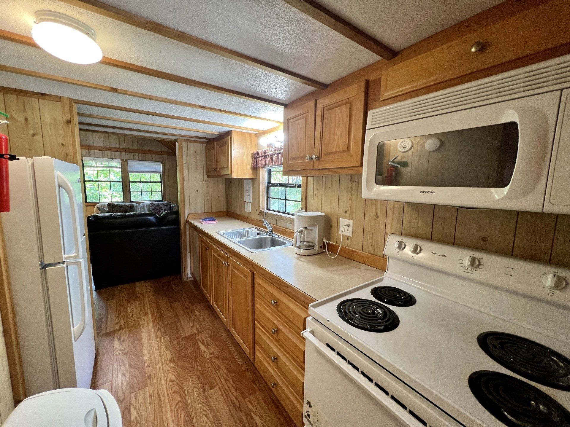 A kitchen with a stove , microwave , refrigerator and sink in humpy fly cabin at copper johns