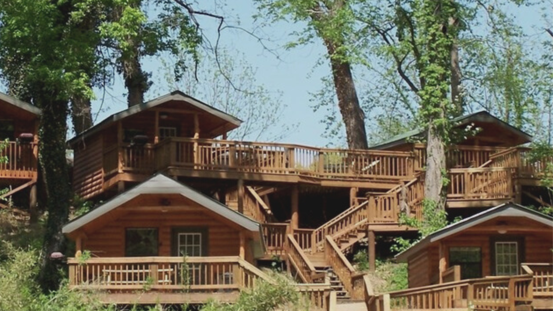 A group of log cabins with stairs leading up to them are surrounded by trees.