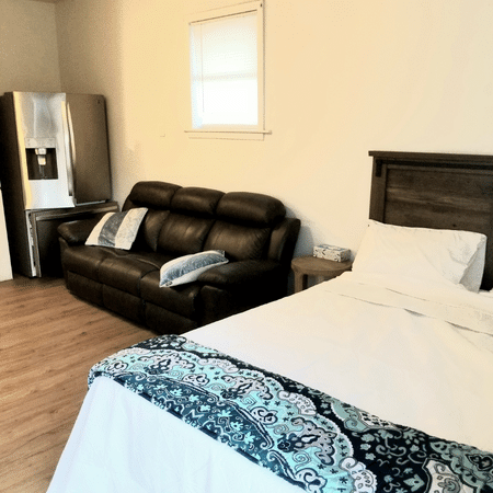 A bedroom with a bed a couch and a refrigerator