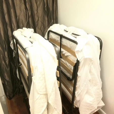 Two folding beds with white sheets on them in a room