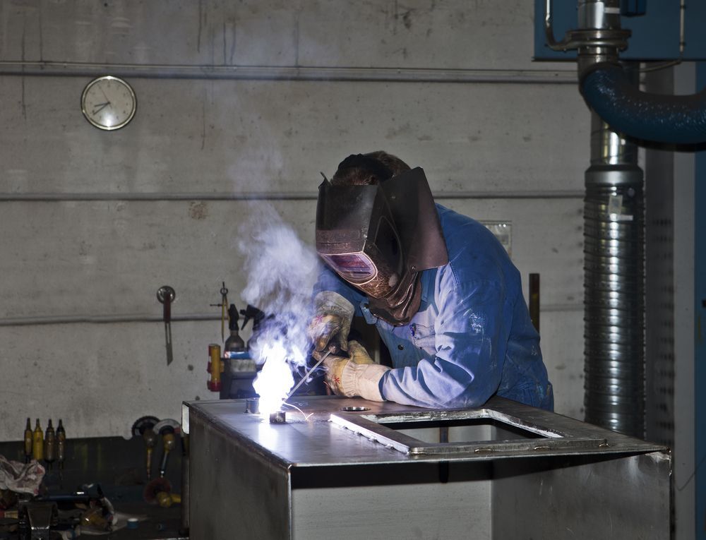A Welder in a Blue Shirt and Mask Works on a Metal Structure Inside a Workshop — Cairns Metal Works in Portsmith, QLD