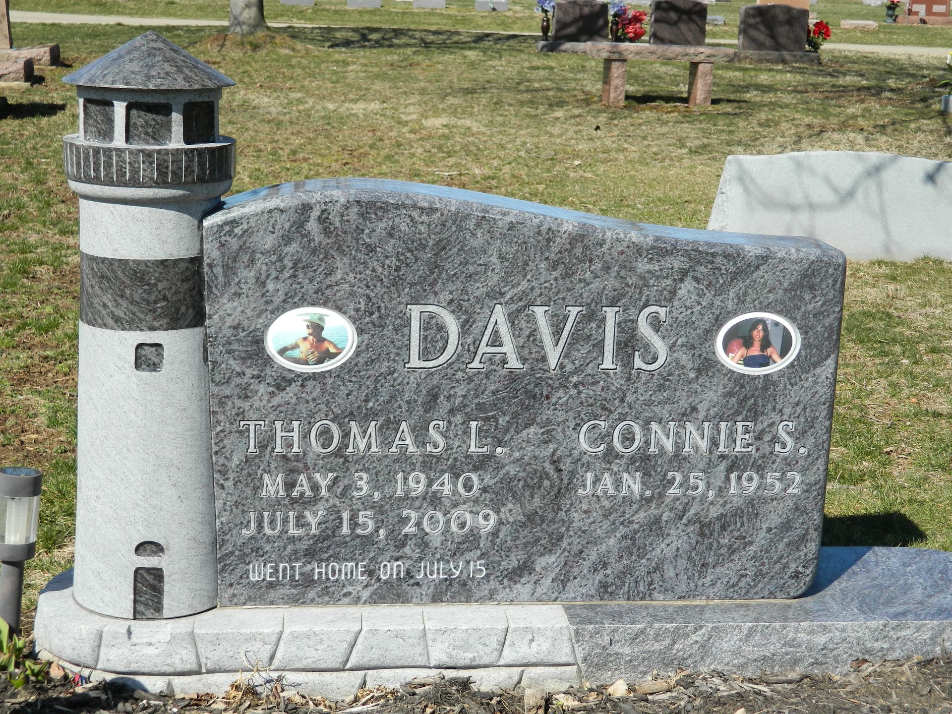 Gray gravestone with lighthouse on left, engraved “DAVIS,” in a grassy cemetery.