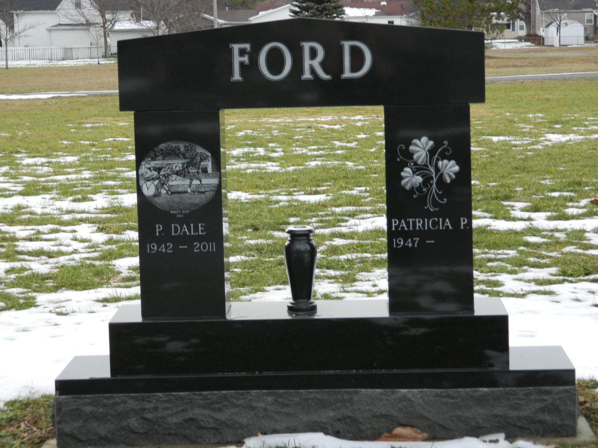 Black FORD gravestone in a snowy cemetery with two engraved panels and a vase in front