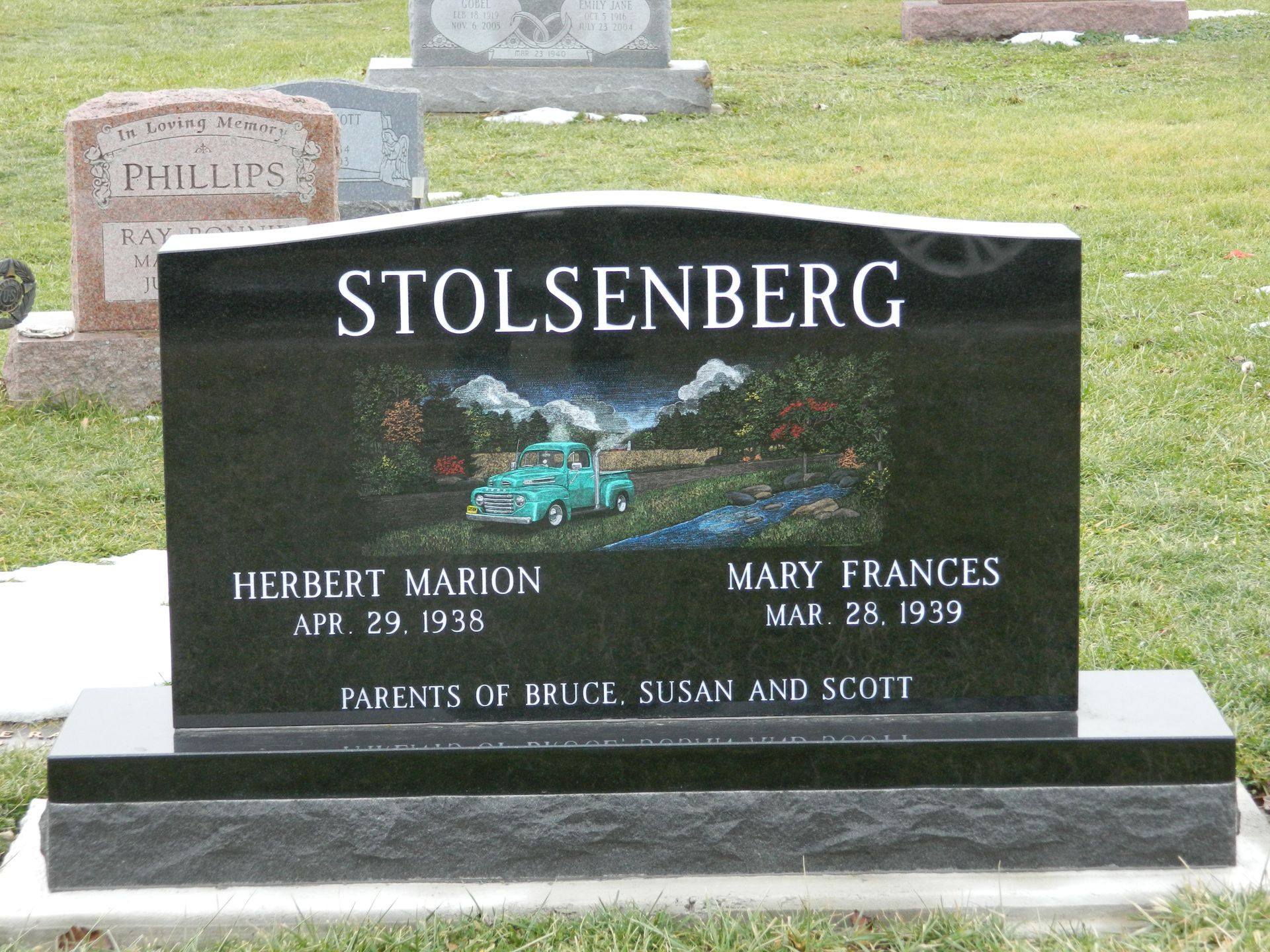Black gravestone with STOLSENBERG name and inscription in a cemetery, with blue flower design
