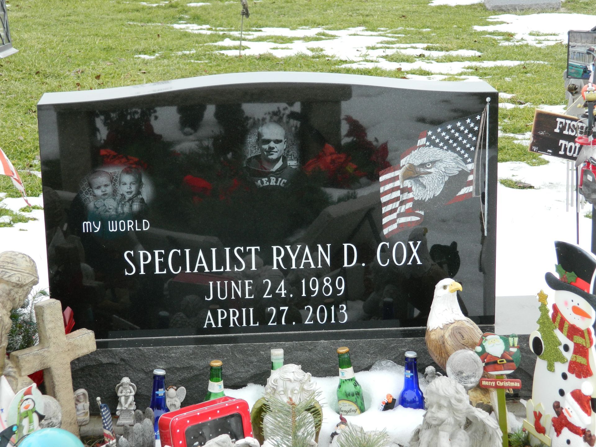 Memorial gravestone for Specialist Ryan D. Cox with red flowers and small flags on a grassy cemetery plot
