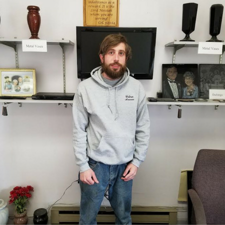 Man standing in a room with wall shelves, a TV, and decorative items behind him.
