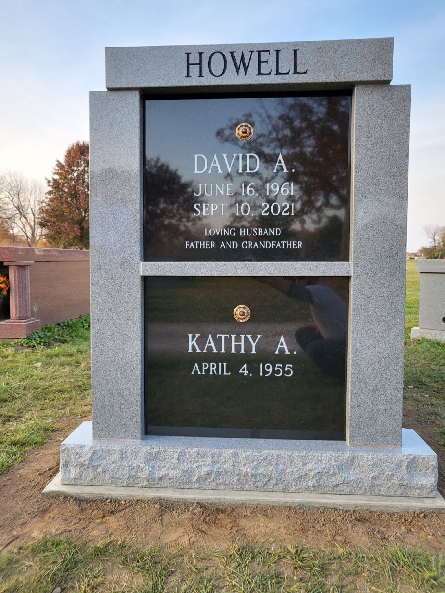 Howell family memorial headstone with two engraved plaques in a cemetery, under overcast light