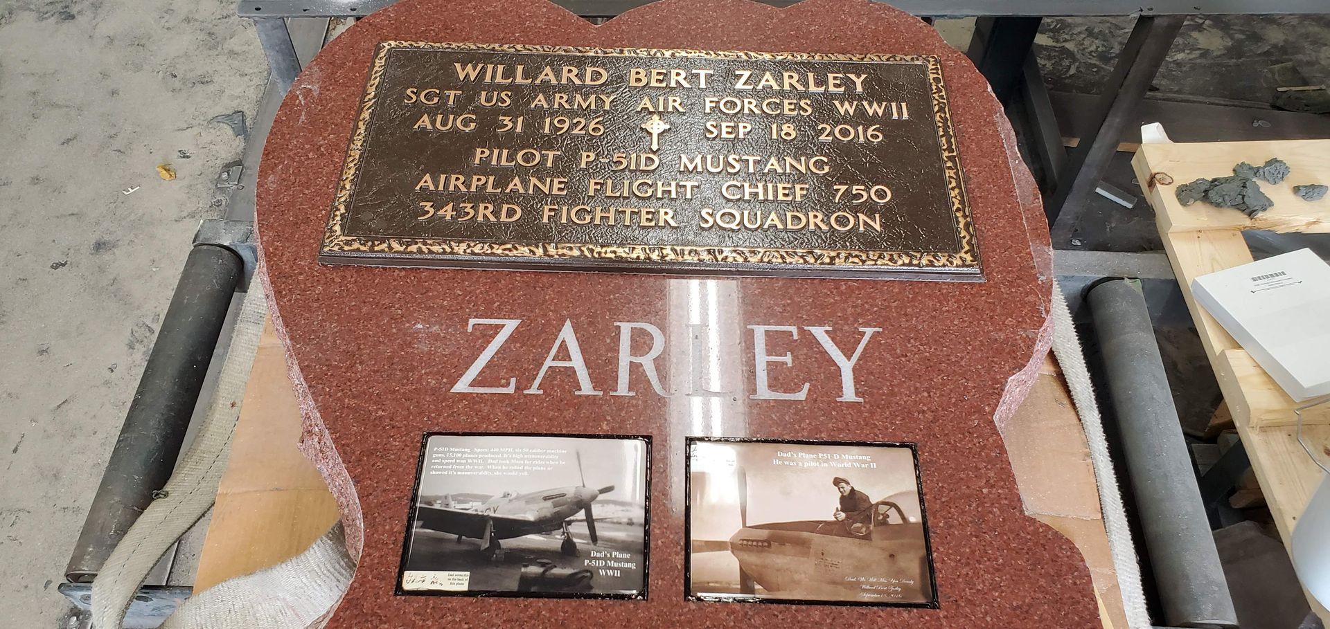 Weathered red memorial plaque on stone, with engraved text, the name “ZARLEY,” and two small photos.