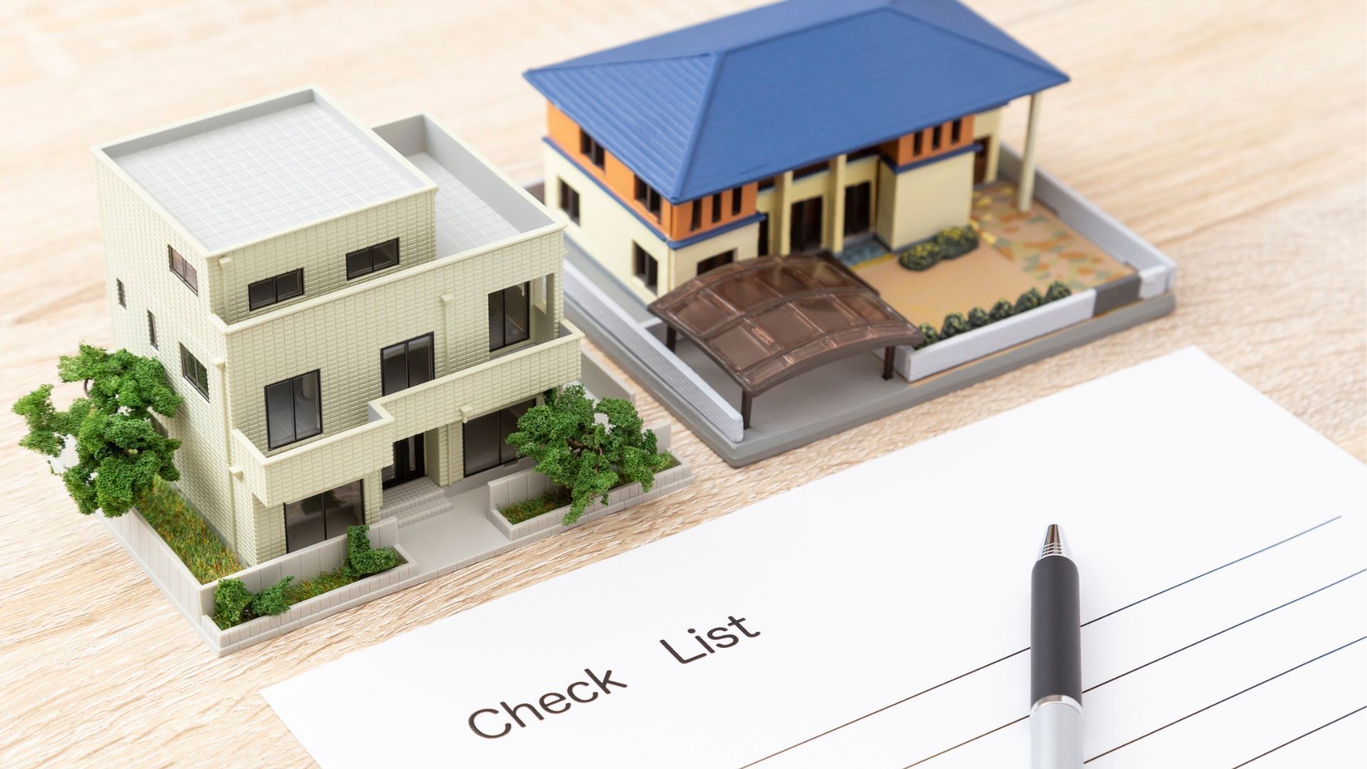 Two architectural house models and a pen resting on a notepad with the heading 