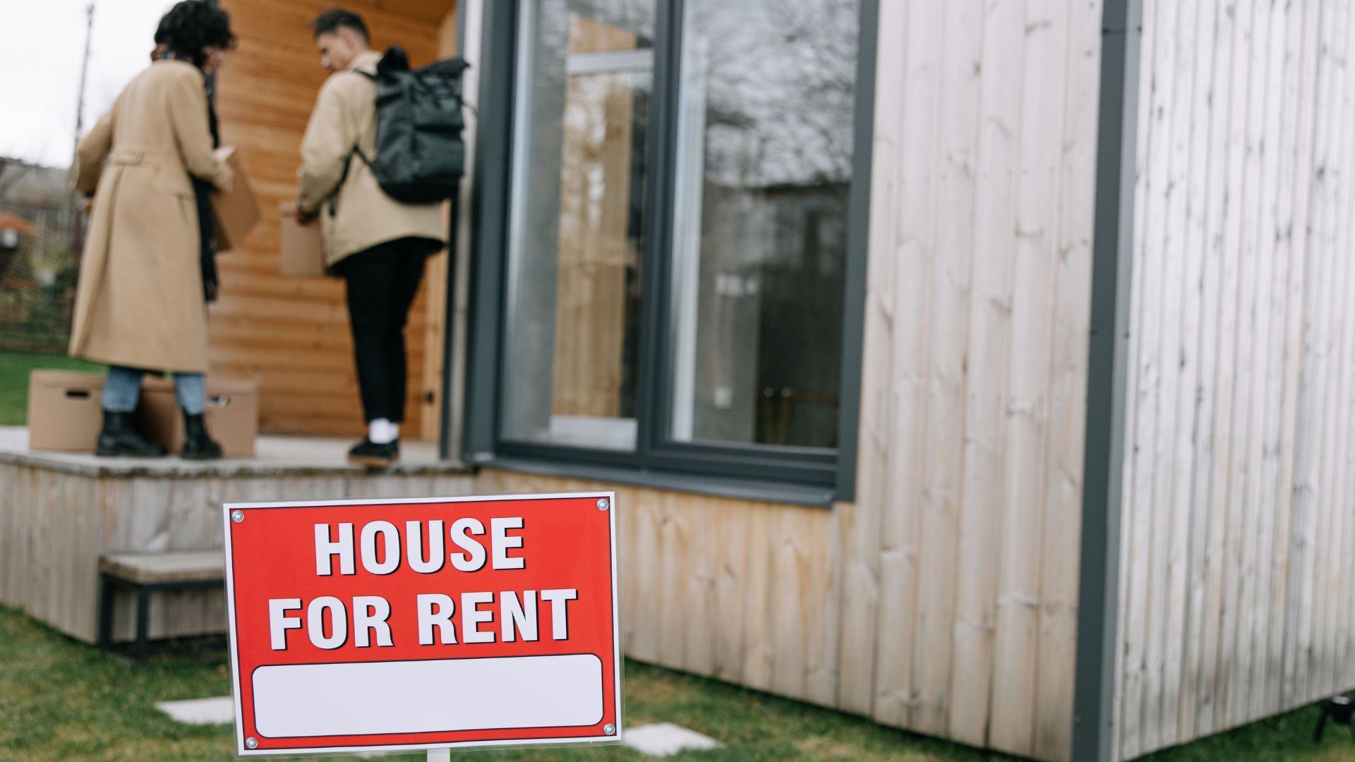 Two people carrying boxes as they move into a rental house