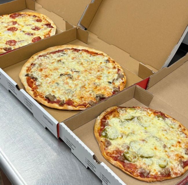 Three pizzas are in cardboard boxes on a table