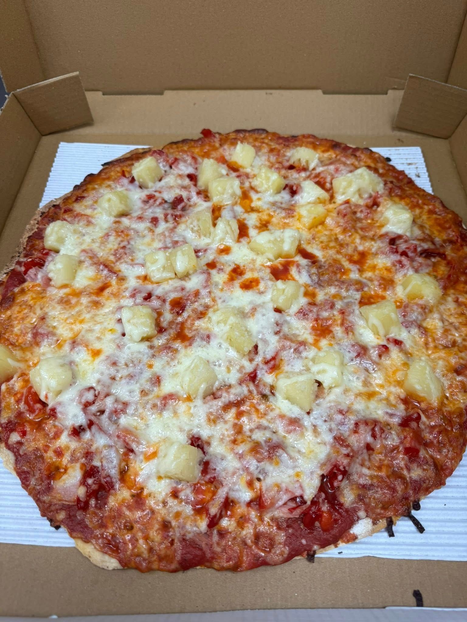 A pizza with pineapple and ham on top is in a cardboard box.