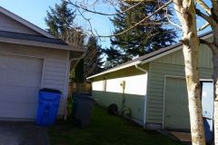 A house with a garage and a blue trash can in front of it.