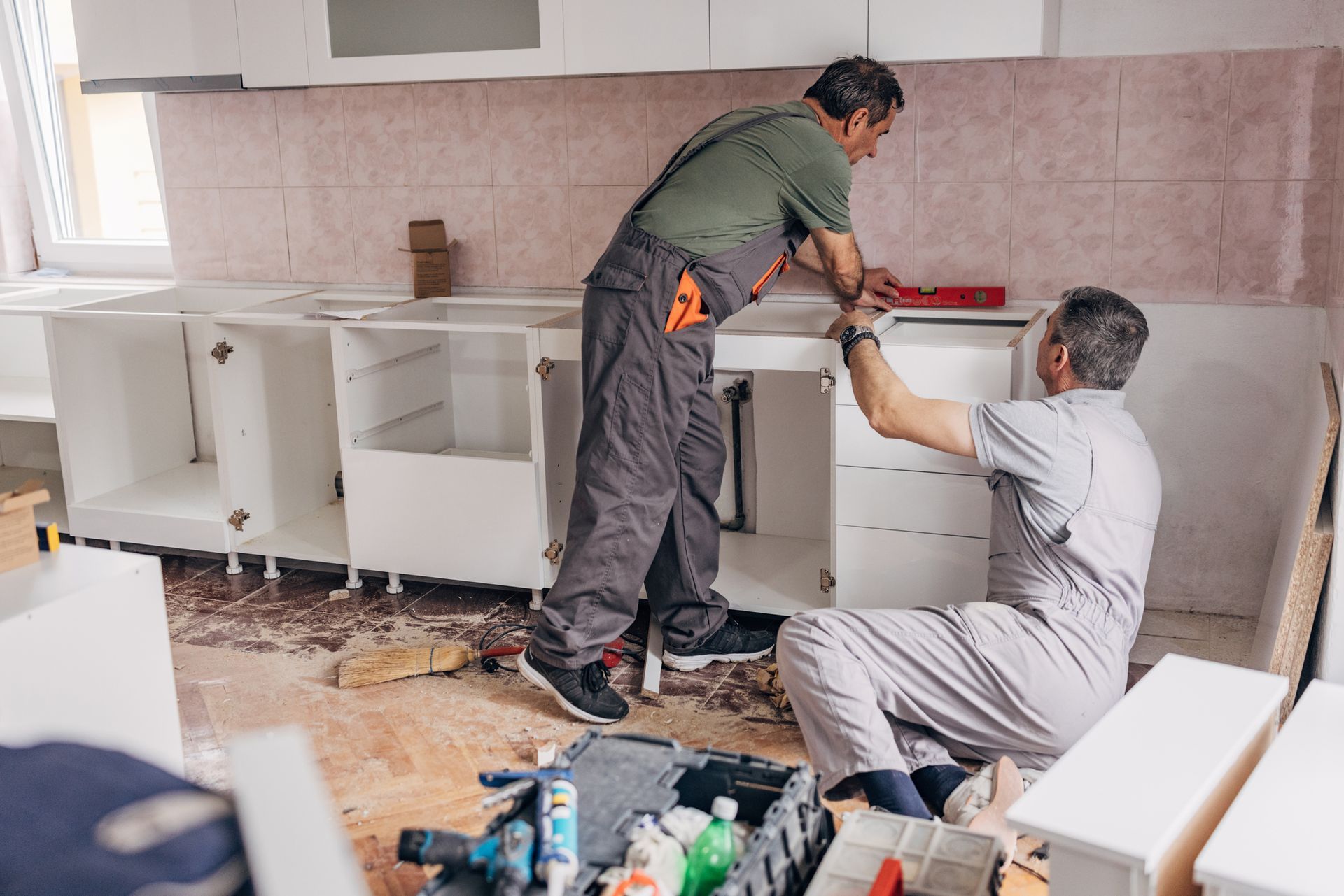 Two workers are installing kitchen cabinets with tools around.