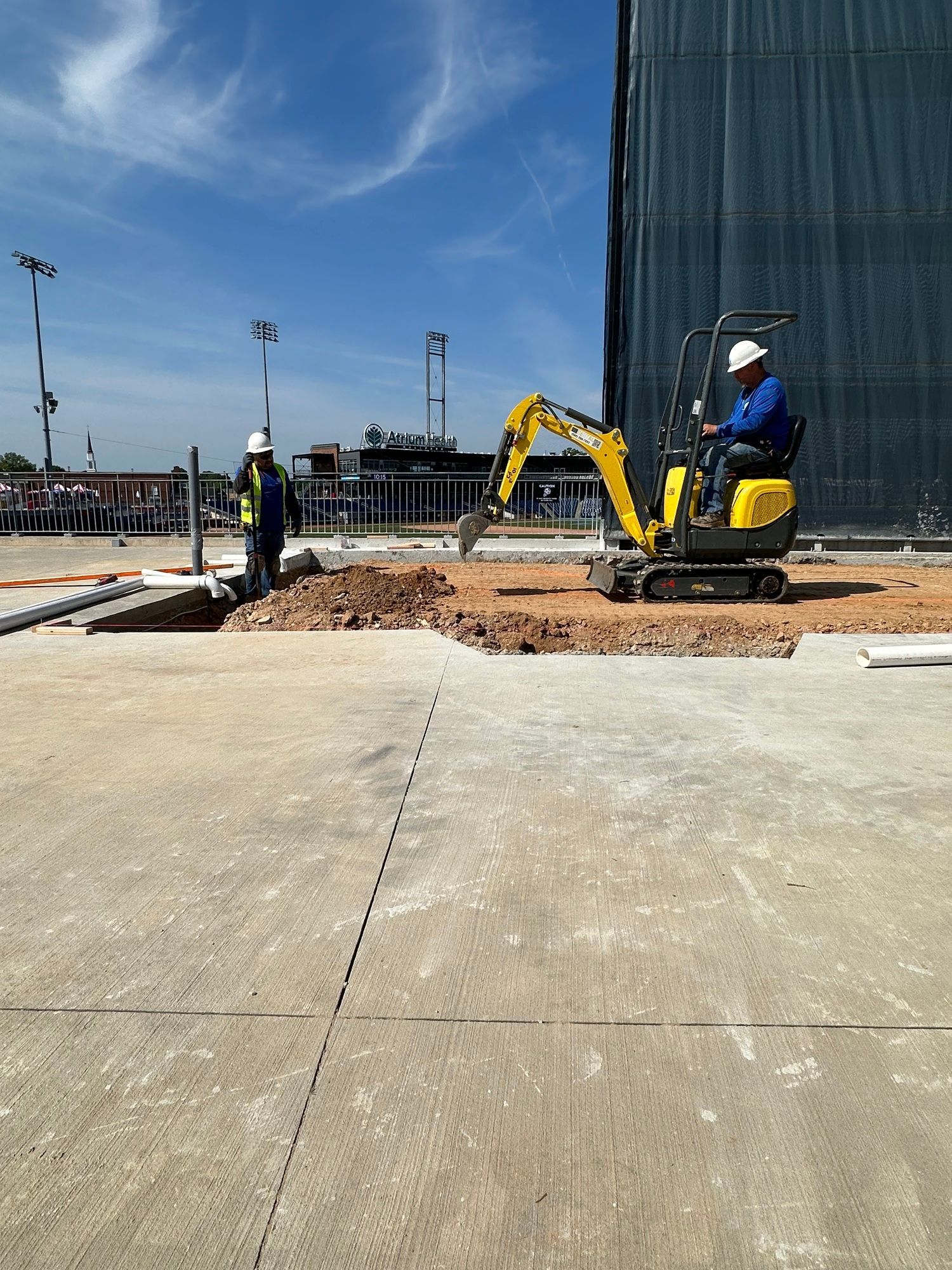 A man is driving a small yellow excavator on a construction site.