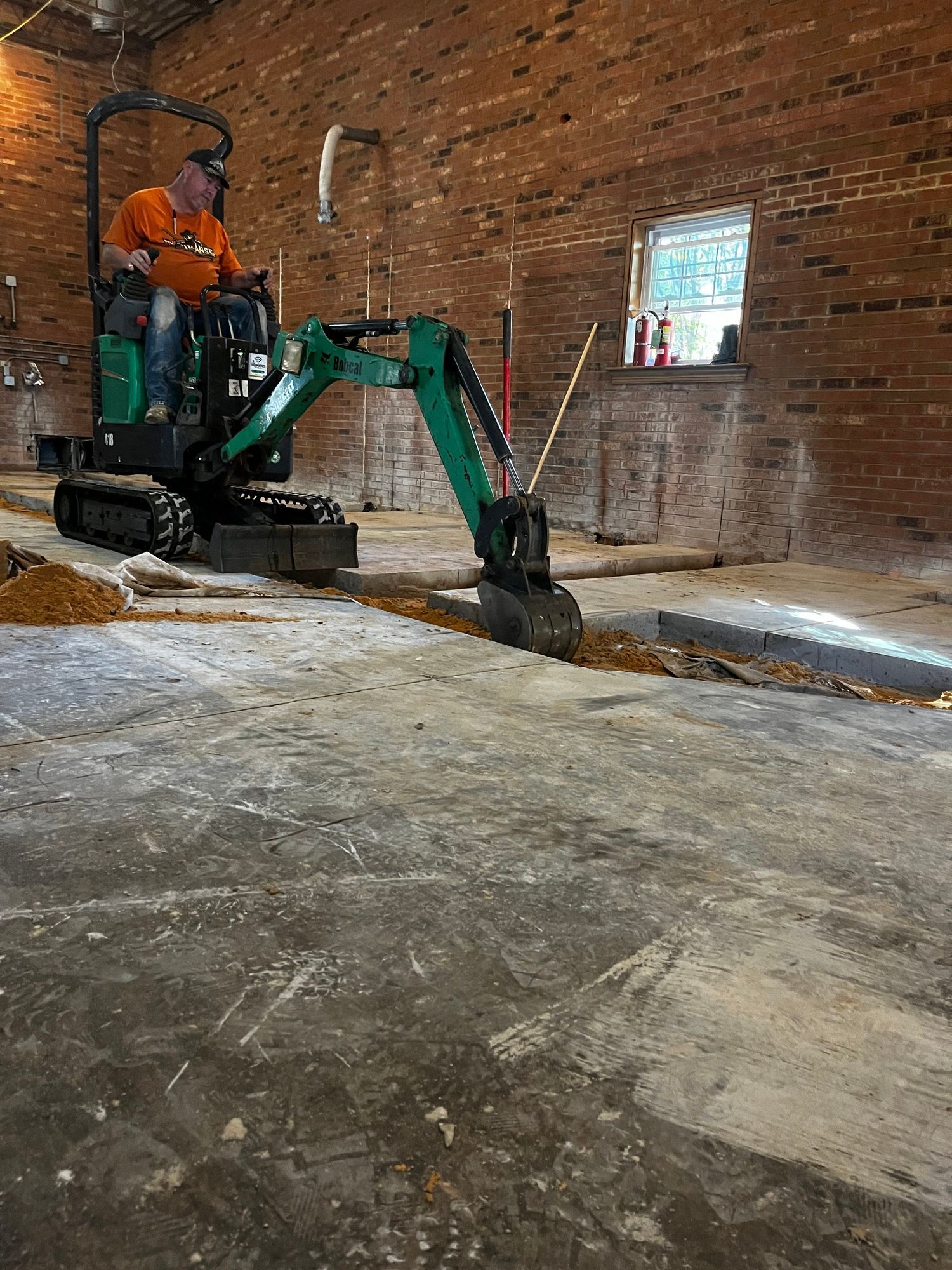 A man is driving a green excavator in a brick building.