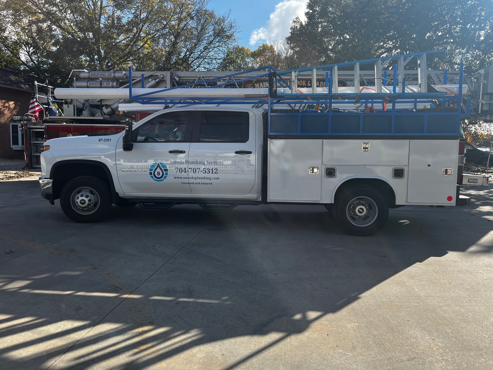 A white truck with a blue ladder on top of it is parked on the side of the road.