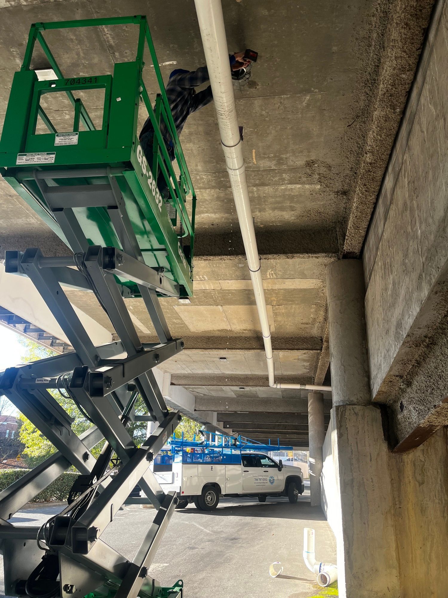 A man is standing on a scissor lift under a bridge.